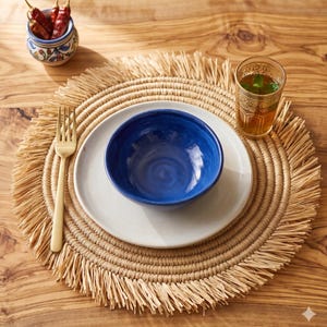 Peut inclure: Une table rustique avec un set de table en osier, une assiette blanche et un bol bleu. Un verre de thé à la menthe et un petit bol de piments rouges sont également présents. Une fourchette dorée est à gauche.