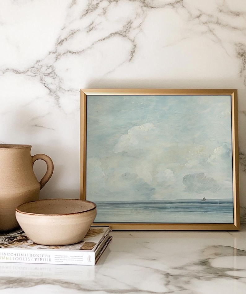 May include: A framed painting of a seascape with a light blue sky and white clouds. The sea is a deep blue and there is a small sailboat in the distance.