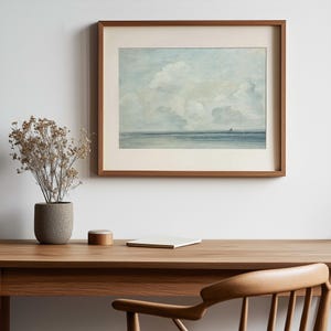 May include: A framed watercolor painting of a seascape with a light blue sky and white clouds. The horizon is a dark blue line with a small island in the distance.
