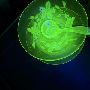 Könnte beinhalten: Ein leuchtend grünes Glasschalen- und Schöpflöffel-Set. Die Schale und der Schöpflöffel haben geätzte Blumen- und Traubenmuster. Das Glas hat eine helle, neongrüne Farbe. Die Schale ist rund mit einem Sockel.
