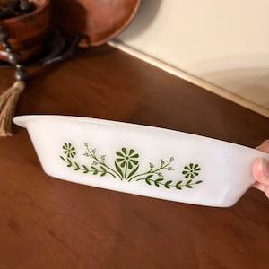 Peut inclure: Plat à four rectangulaire blanc avec un motif floral vert. Le plat a une forme légèrement incurvée et est fait d'un matériau brillant. Le motif floral vert comprend des fleurs et des feuilles stylisées. Le plat est probablement vintage.