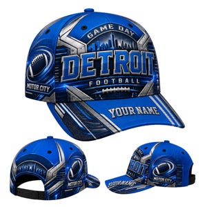 Pode incluir: Um boné de beisebol azul com um gráfico do horizonte de Detroit, uma bola de futebol americano e o texto "GAME DAY", "DETROIT", "FOOTBALL", "MOTOR CITY" e "YOUR NAME". O design inclui detalhes em prata metálico e aba curva.