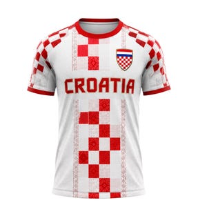 Pu&ograve; includere: Maglia da calcio della Croazia bianca e rossa. La maglia presenta un motivo a scacchi rossi e bianchi sulle maniche e uno stemma. La parola "CROATIA" &egrave; stampata in rosso sul petto.