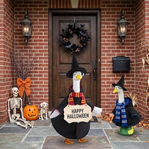 May include: Two white goose figurines dressed in black wizard hats, capes, and round glasses. The larger goose wears a red and yellow striped scarf and holds a sign that reads HAPPY HALLOWEEN. The smaller goose wears a blue and silver striped scarf.