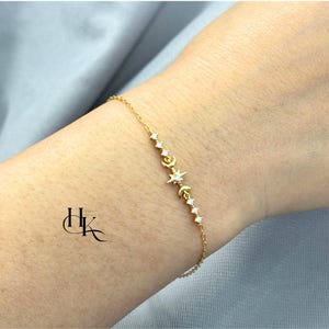 Puede incluir: Una delicada pulsera dorada con un diseño celestial. La pulsera incluye una serie de pequeños cristales brillantes, medias lunas y una estrella. La pulsera se lleva en la muñeca, mostrando sus intrincados detalles y su elegante diseño.