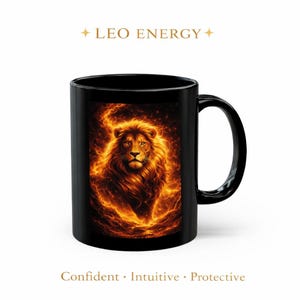 Könnte beinhalten: Schwarze Keramik-Tasse mit einer detaillierten Illustration eines Löwen mit feuriger Mähne und Flammen. Der Text "LEO ENERGY" steht über dem Löwen, darunter "Confident • Intuitive • Protective". Ein auffälliges Design.