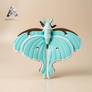 Puede incluir: Escultura decorativa de polilla en azul claro, marrón y blanco. Las alas tienen una apariencia texturizada con recortes circulares. La escultura tiene un diseño caprichoso. El texto "ALOHASOFT" está en la esquina superior izquierda.