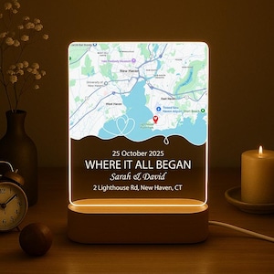 May include: An illuminated night light with a map of New Haven, CT. The light displays the text "WHERE IT ALL BEGAN" and a date. The base is wooden, and the light is on a table with a candle and clock. The light is plugged in.