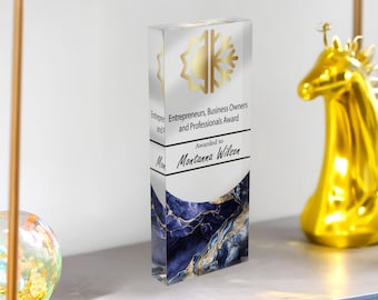 Puede incluir: Un premio de acrílico transparente con detalles dorados. El premio rectangular presenta un emblema dorado y el texto "Entrepreneurs, Business Owners and Professionals Award" y "Awarded to Montanna Wilson." La base tiene un diseño veteado azul y dorado.