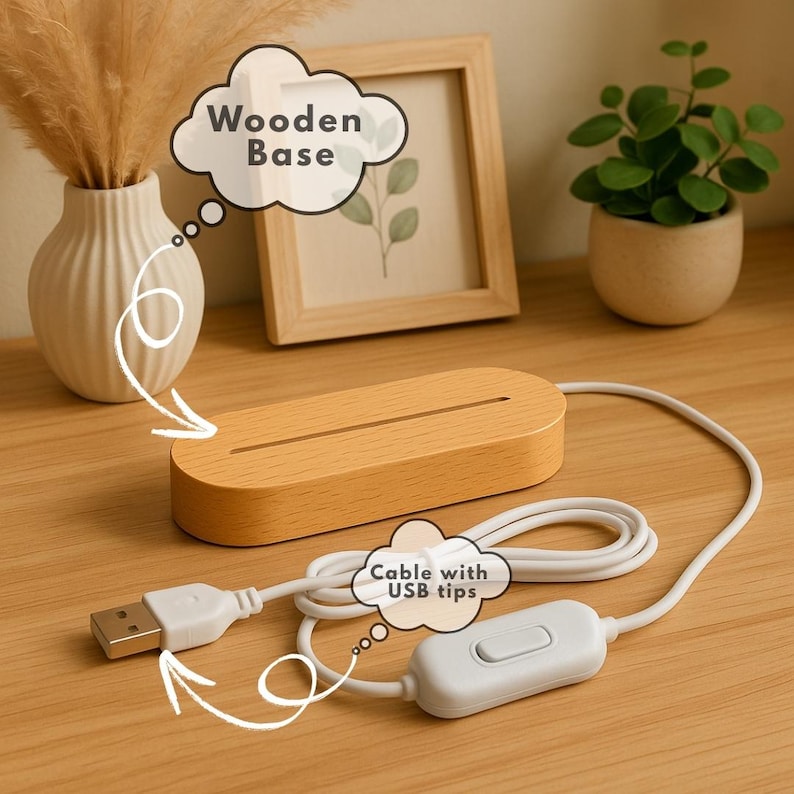 May include: A light-colored wooden base with a slot, connected to a white cable with a USB tip and an on/off switch. The base is rectangular with rounded edges. The background includes a framed picture, a vase, and a small potted plant.