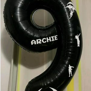 May include: Black number 9 balloon with white Fortnite logo and graphics. The name "ARCHIE" is printed in white. The balloon is a party decoration.