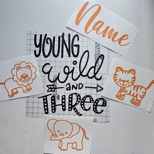 May include: A selection of orange and black vinyl decals. The decals feature a lion, tiger, elephant, and the phrase "Young Wild and Three" with an arrow. An additional decal says "Name" in orange script.