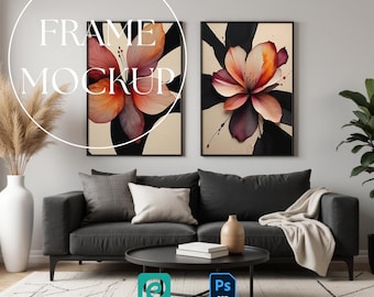May include: Two rectangular wall art prints in black frames featuring abstract floral illustrations with orange, pink, and black petals on a cream background, displayed above a dark gray sofa with cushions and a throw blanket in a living room.