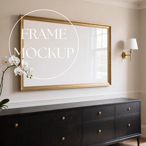 Può includere: Mockup di arte murale rettangolare con cornice dorata e testo bianco "FRAME MOCKUP". La cornice è appesa sopra un comò nero con pomelli dorati. Sono visibili anche un'orchidea bianca e un'applique dorata.