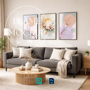 May include: A set of three vertical wall art prints in black frames featuring watercolor cherry blossom branches and circular sun motifs in soft pastel tones of pink, orange, and blue, displayed above a dark gray sofa with neutral pillows.