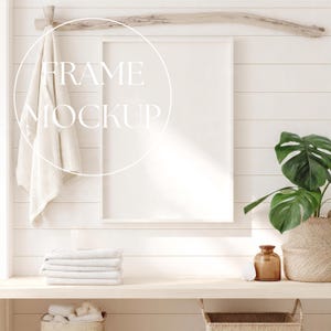 May include: A white frame mockup with the text "FRAME MOCKUP" overlaid. A folded white towel hangs from a wooden beam. A stack of white towels and a potted plant are on a wooden shelf.