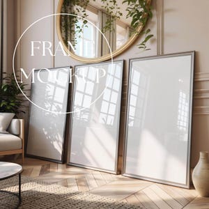 Könnte beinhalten: Drei große, vertikale Bilderrahmen mit silberfarbenen Rändern lehnen an einer Wand. Die Rahmen sind leer, mit dem Text "FRAME MOCKUP" in Weiß über dem Bild. Ein runder goldener Spiegel und eine beige Vase sind ebenfalls zu sehen.