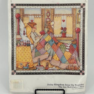 May include: Daisy Kingdom iron-on transfer featuring a watercolor illustration of a person reading in bed. The scene includes a colorful quilt, a window, and the text "The Get Well Fairy".