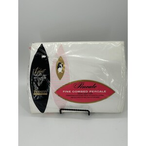 May include: A white 100% cotton double bed sheet in plastic packaging. The label features the text Penney's, Fine Combed Percale, and 1 sheet double bed 81 x 108 inches. The packaging includes black, pink, and white graphic design elements.