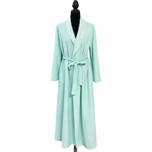May include: A floor-length, light mint green robe featuring long sleeves, a shawl collar with delicate pink and green floral embroidery, and a matching fabric tie belt at the waist. The garment is displayed on a black mannequin torso.