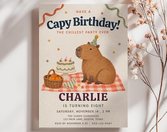 May include: A rectangular birthday invitation card featuring a brown capybara wearing a green party hat on a red and white checkered picnic blanket. The text reads: Have a Capy Birthday! The Chillest Party Ever, Charlie is turning eight, Saturday, November 14, 2 PM, The Sunny Clubhouse, 123 Palm Lane, Austin, Texas, RSVP by November 3 at 555-123-4567.