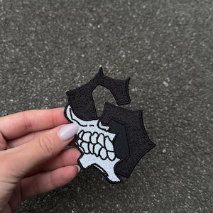 May include: Black and white embroidered patch in the shape of the letter "S" with a skull design. The skull is white with black detailing, and the letter is outlined in black.