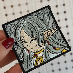 May include: Embroidered patch featuring a stylized anime character with long, silver hair and pointed ears. The character is depicted with a neutral expression, wearing a white and gold outfit. The patch has a black border and is square-shaped.