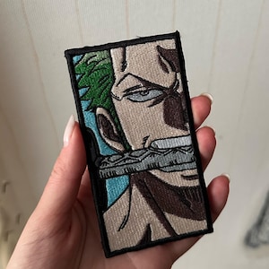 May include: Embroidered patch featuring a character from the anime series. The patch depicts a side profile of a character with green hair, a stern expression, and a sword in their mouth. The patch has a black border.