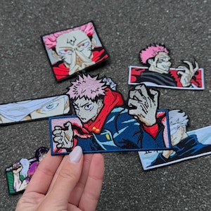 May include: A selection of embroidered anime character patches. The patches depict characters with pink and white hair, dressed in blue and red attire. The patches are rectangular and square, with detailed facial expressions and dynamic poses.