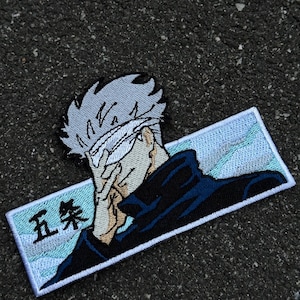 May include: Embroidered patch depicting a character with white hair and a blindfold, covering their face with a hand. The patch has a rectangular border with Japanese text and a blue and white background.