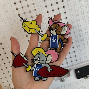 May include: Three embroidered patches featuring cartoon mice. One mouse holds a cheese wedge, another wears a pink cowboy hat, and the third holds a red object. The patches are colorful and detailed, suitable for clothing or accessories.