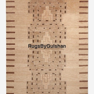 May include: A beige and brown rectangular rug with a geometric design. The rug has a central pattern of stepped shapes and horizontal stripes. The text "RugsByGulshan" is printed on the rug.