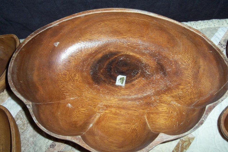 Peut inclure: Un grand bol en bois avec un bord festonn&eacute; unique. Le bol est fait d'un bois brun moyen chaud avec des motifs de grain visibles. L'int&eacute;rieur pr&eacute;sente un motif tourbillonnant plus fonc&eacute;. Une petite &eacute;tiquette est visible au centre.