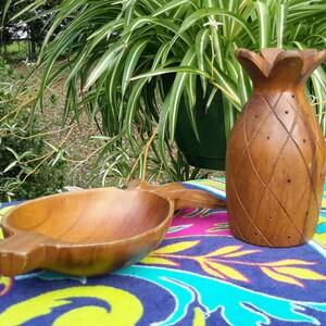 May include: Two wooden bowls in the shape of a pineapple. The larger bowl is a serving bowl with a handle. The smaller bowl is a decorative bowl. Both bowls are made of dark wood and have a natural finish.