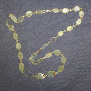 May include: A gold chain necklace with oval-shaped green stones. The necklace is laid out on a dark gray surface.