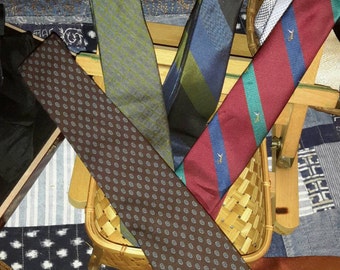 May include: A collection of neckties in various patterns and colors, displayed in a small wooden easel and a woven basket. The ties include designs with paisley, stripes, and geometric shapes. Colors include brown, green, blue, and red.
