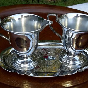 May include: A silver creamer and sugar set with a matching tray. The set is on a wooden surface.