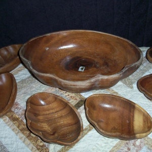 Peut inclure: Un ensemble de bols en bois faits &agrave; la main de diff&eacute;rentes tailles et formes. Les bols sont de couleur marron chaud avec le grain du bois visible. Le plus grand bol a un bord festonn&eacute; unique. Les bols sont dispos&eacute;s sur une surface &agrave; motifs.