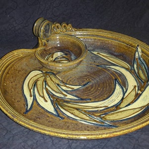 May include: A brown ceramic serving dish with a smaller bowl attached. The dish is decorated with a swirling pattern of white and brown leaves.