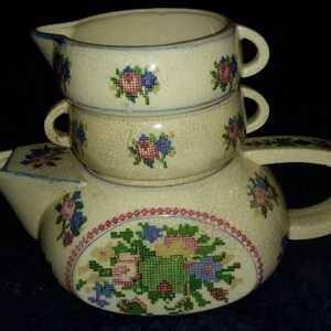 May include: A set of three vintage ceramic cups with floral designs. The cups are stacked on top of each other, with the largest cup at the bottom and the smallest cup at the top. The cups are decorated with a white background and colorful floral patterns.
