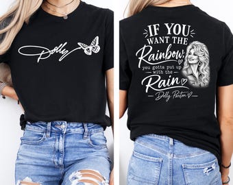 May include: A black t-shirt featuring a white graphic on the front with the word Dolly in script and a butterfly. The back of the shirt displays a white graphic of Dolly Parton with the text If you want the rainbow, you gotta put up with the rain.