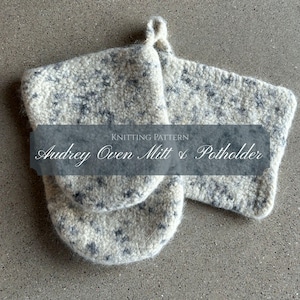 May include: A knitted oven mitt and potholder set in a speckled white and gray pattern. The text "Audrey Oven Mitt & Potholder" is displayed on a banner across the image. The oven mitt has a loop for hanging.