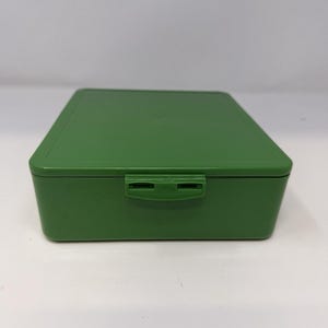 May include: A solid green rectangular box with a hinged lid and a clasp closure. The box is made of a smooth, matte material. The box is empty and ready to be filled with small items.