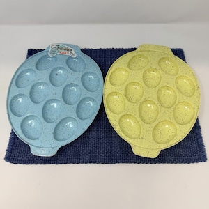 Può includere: Due piatti ovali, uno azzurro e uno giallo, ciascuno con motivi maculati e rientranze per contenere il cibo. Il piatto blu ha un adesivo che dice "Sprinkles zak!". I piatti sono posti su una superficie blu scuro strutturata.