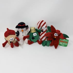 Puede incluir: Colección de peluches con temática navideña, que incluye un muñeco de nieve, un bastón de caramelo, una flor de pascua, un personaje de judía verde y un cascanueces. Cada juguete tiene una cara sonriente y está hecho de tela suave. Los juguetes están diseñados con colores brillantes y detalles festivos.