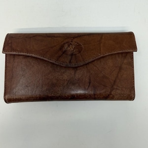 May include: A brown leather wallet with a flap closure. The wallet has a textured surface and a circular embossed design on the front. The wallet is rectangular and appears to be made of genuine leather.