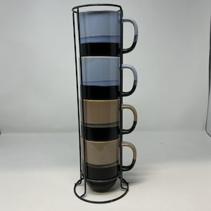 May include: A set of four stacked ceramic mugs in a black metal stand. The mugs are blue, black, and tan with a modern design. The mugs have a capacity of approximately 12 ounces.