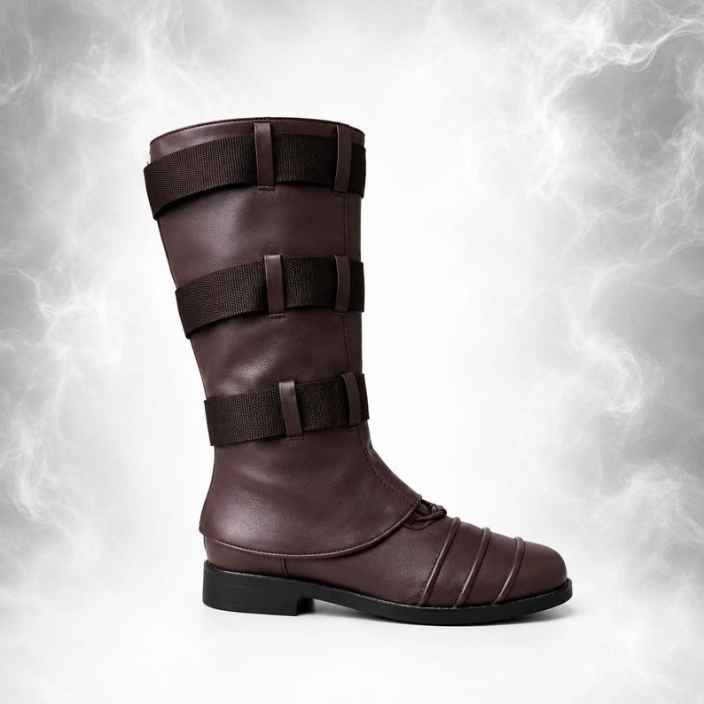 May include: A mid-calf dark brown boot featuring three horizontal dark brown fabric straps across the shaft, each secured with loops. The toe area displays a series of raised horizontal lines, and the boot is finished with a flat black sole.