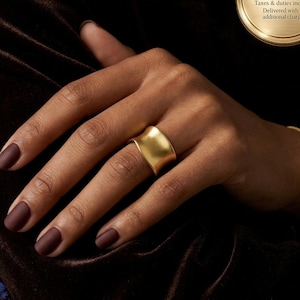 Anillo llamativo en oro con diseño de banda ancha y gruesa ajustable.