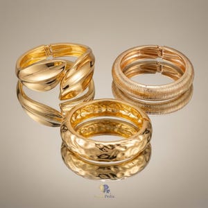May include: Three gold-toned metal bracelets. One features a smooth, leaf-like overlapping design. Another is a circular bangle with a fine, ribbed texture. The third is a circular bangle with a hammered, irregular surface. All have hinged closures.